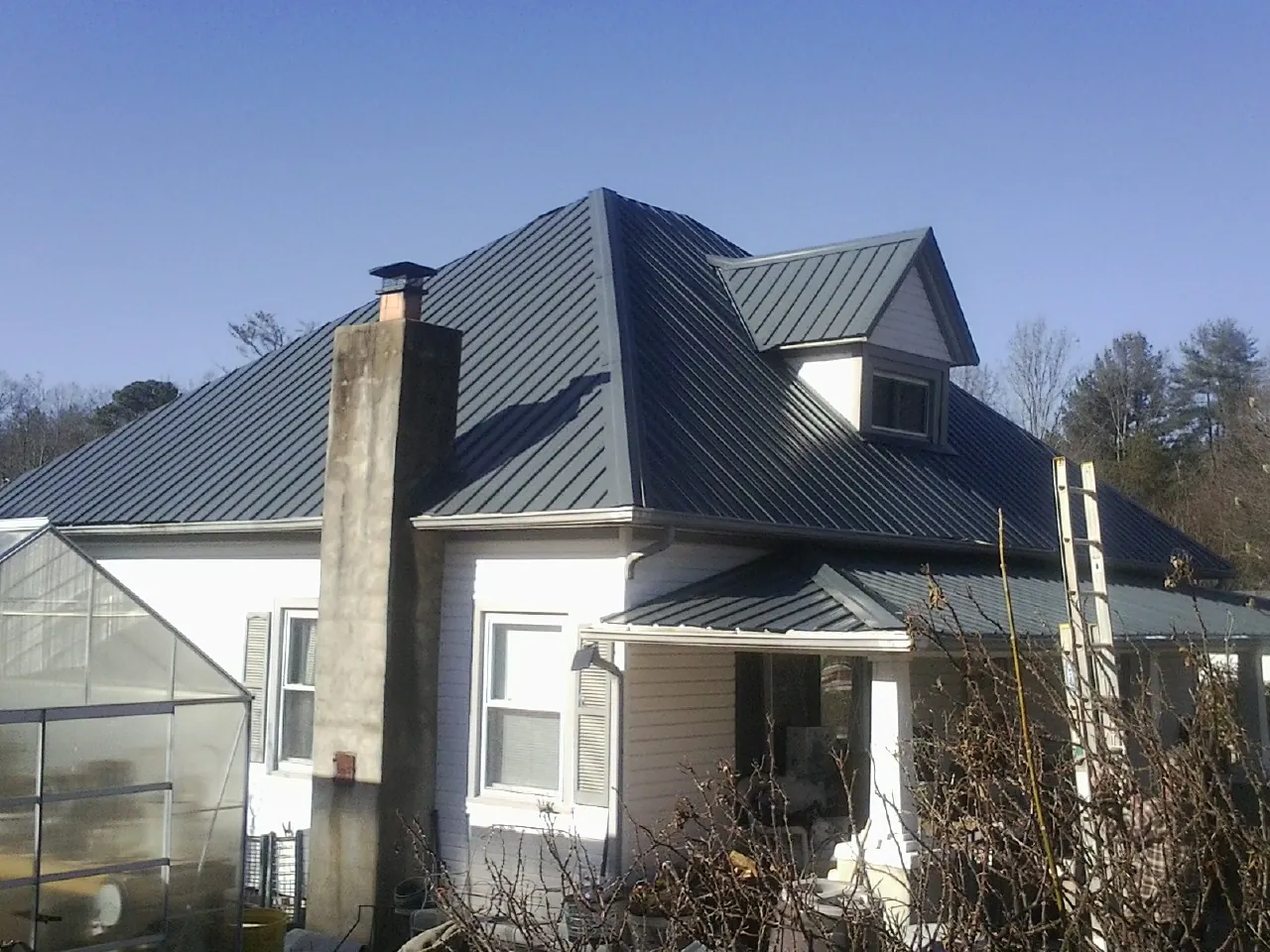 Dark blue standing seam metal roof on a white farmhouse with dormer — Slate & Tile Roof Repair by Roofing Brothers in Tunkhannock