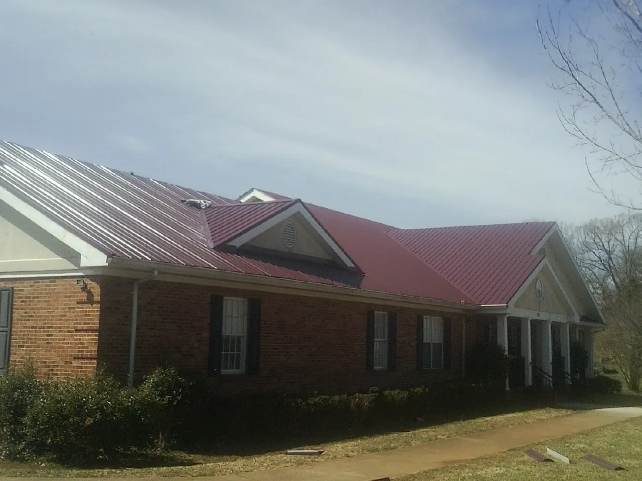Red metal roof with gabled entries on a long brick building, from a Hail Damage Roof Repair job in Tunkhannock