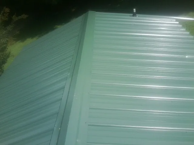 New green metal panels meeting at the ridge of a roof — Flat Roof Repair work by our crew in Tunkhannock