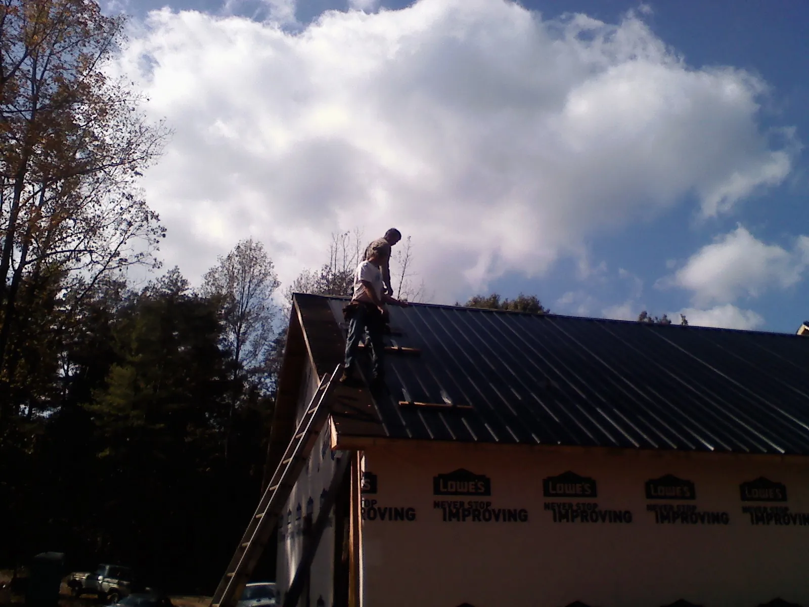 Roofer fastening dark metal panels high against a cloudy sky, from a Roof Inspection job in Tunkhannock