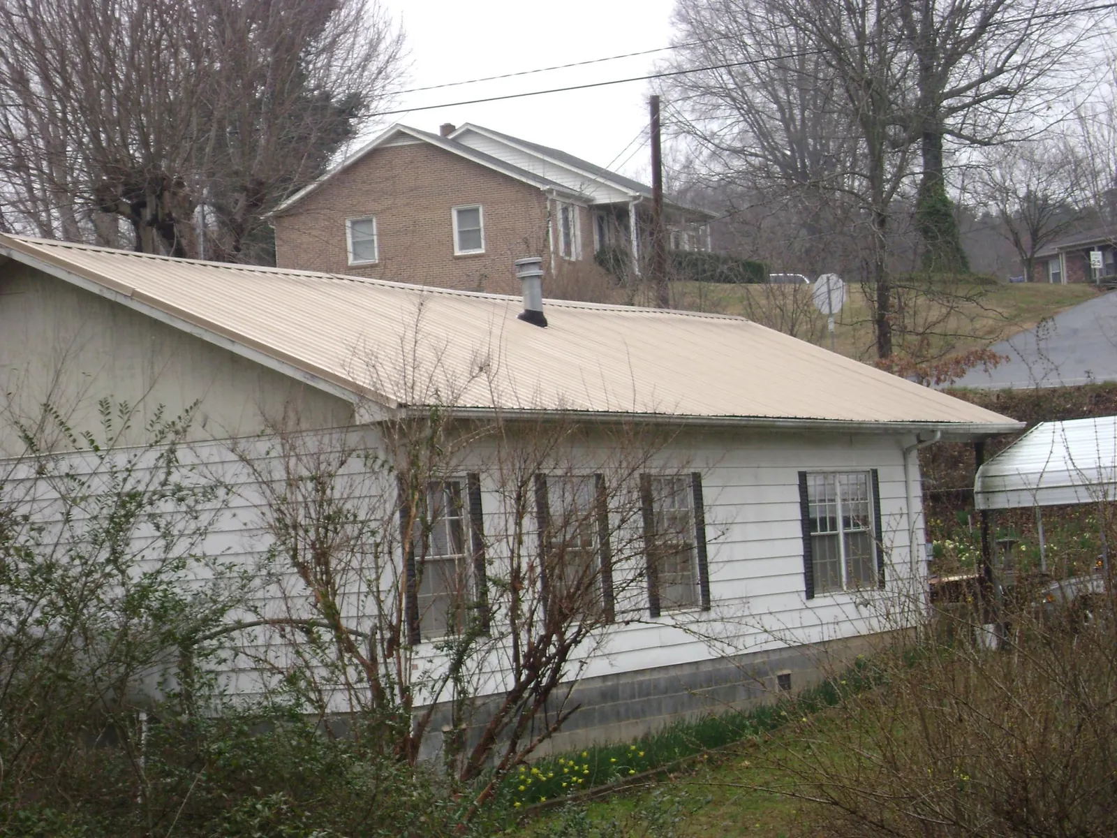 Tan metal roof on a white sided house set into a hillside — Commercial Roofing by Roofing Brothers in Tunkhannock